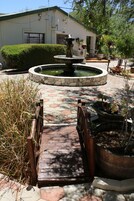 Un patio con una fuente, un puente de madera y plantas en macetas.