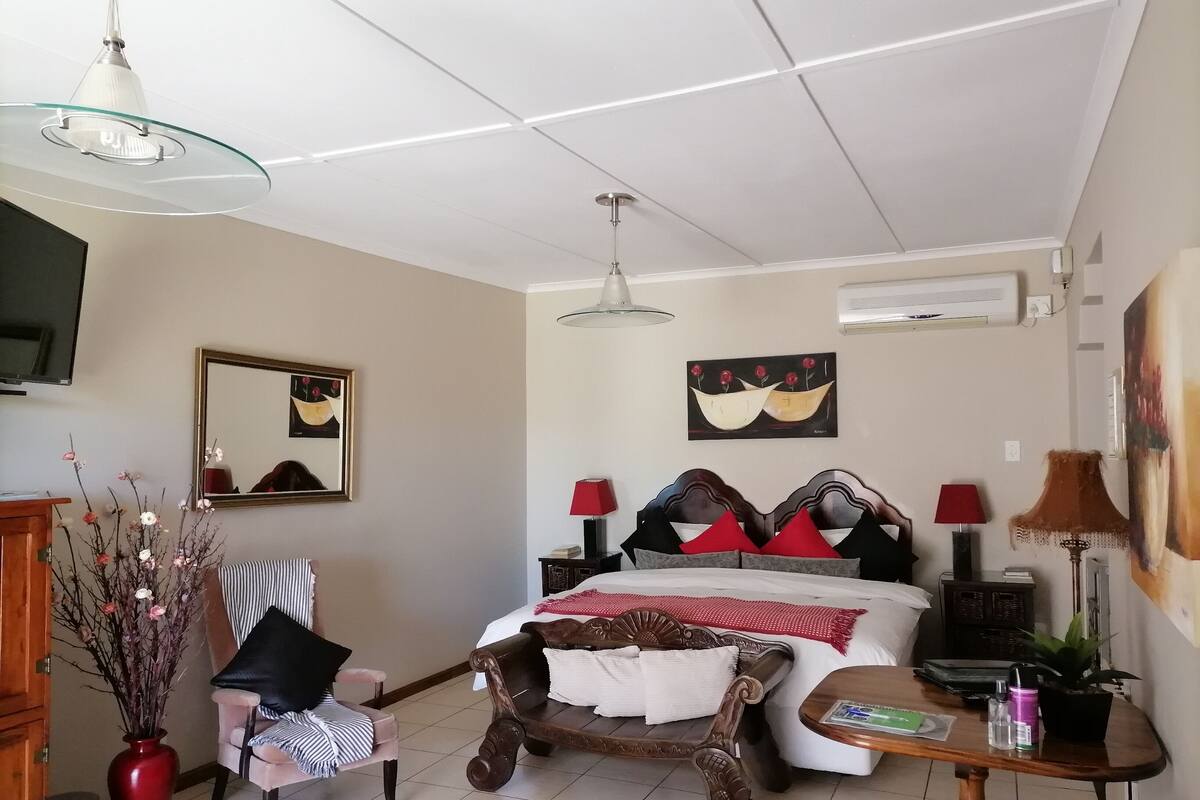 A bedroom with a bed, bedside tables, a chair, a desk, a TV, a mirror, and a vase with flowers.