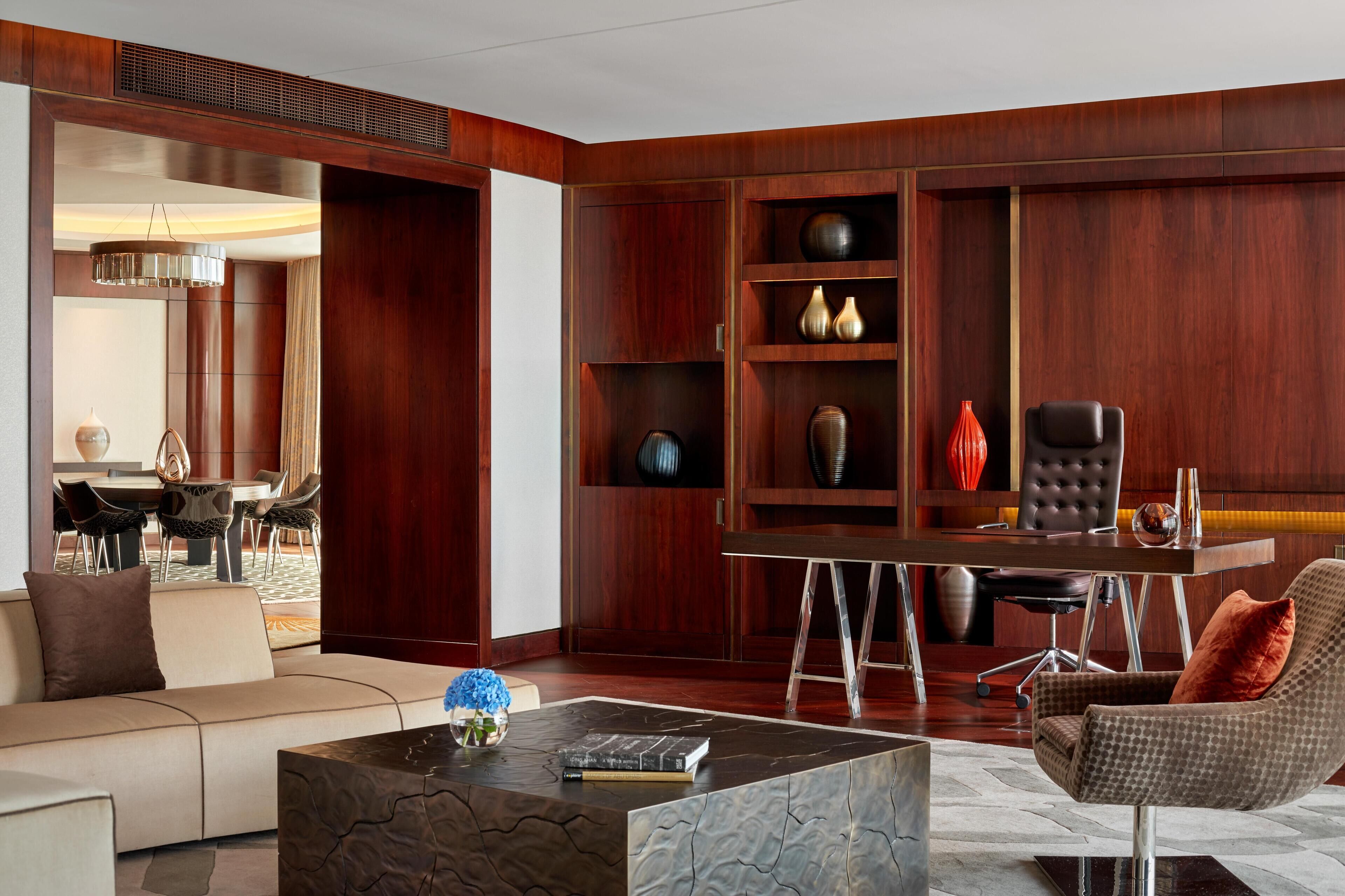 Una sala de estar moderna con un sofá, una mesa de centro, una zona de comedor con mesa y sillas, y un mueble de madera empotrado con objetos decorativos.