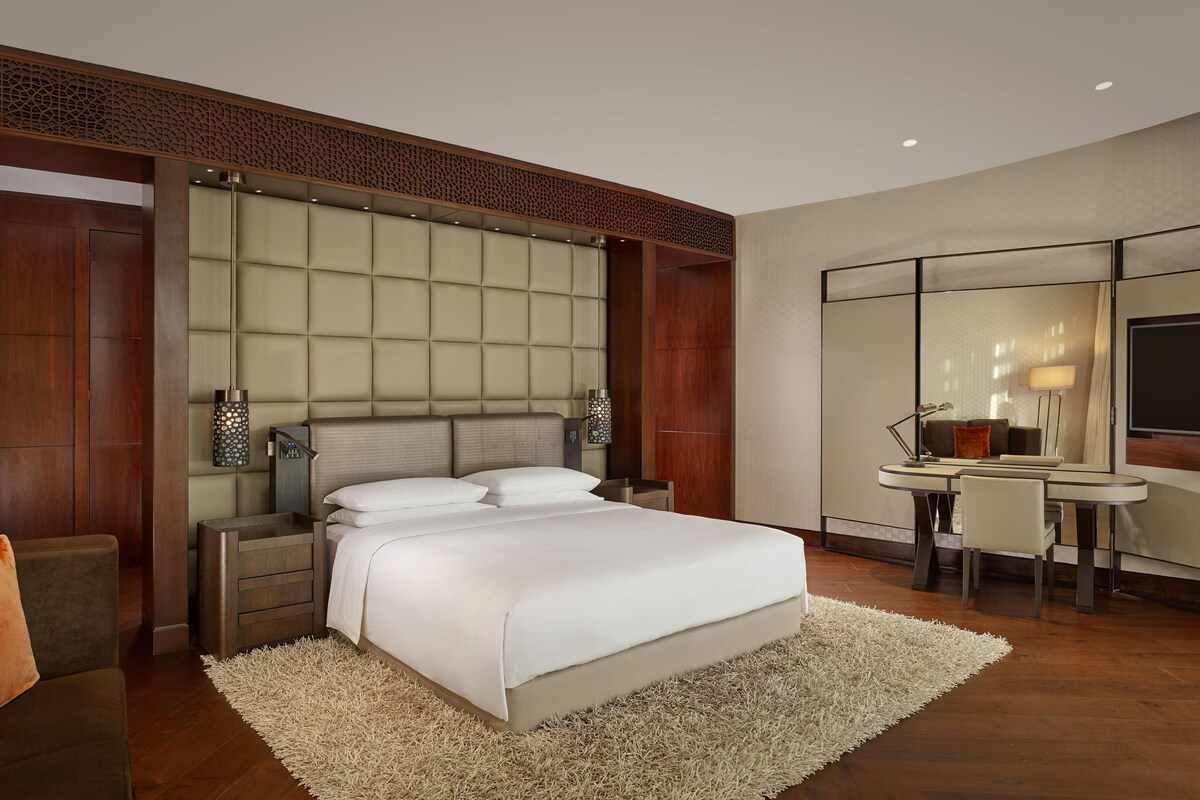 A hotel room with a large bed, a desk with a chair, a mirror, and a TV.