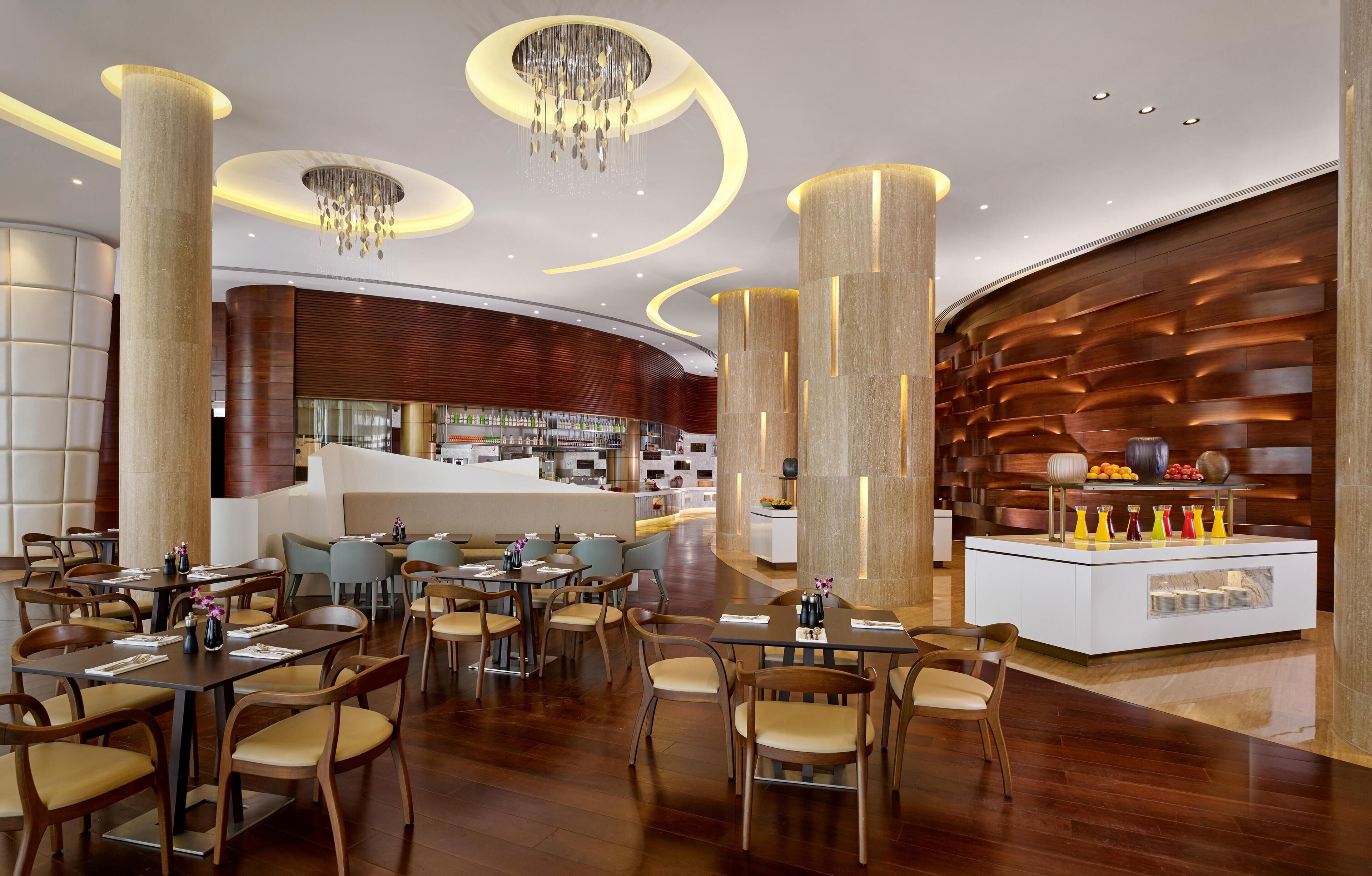 Een modern restaurant met houten vloeren, ronde tafels en stoelen. Achtergrond heeft hoge pilaren en een bar.