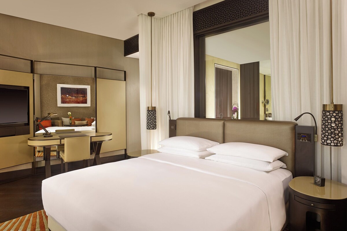 A hotel room with a bed, a desk, a chair, a TV, and a large mirror.