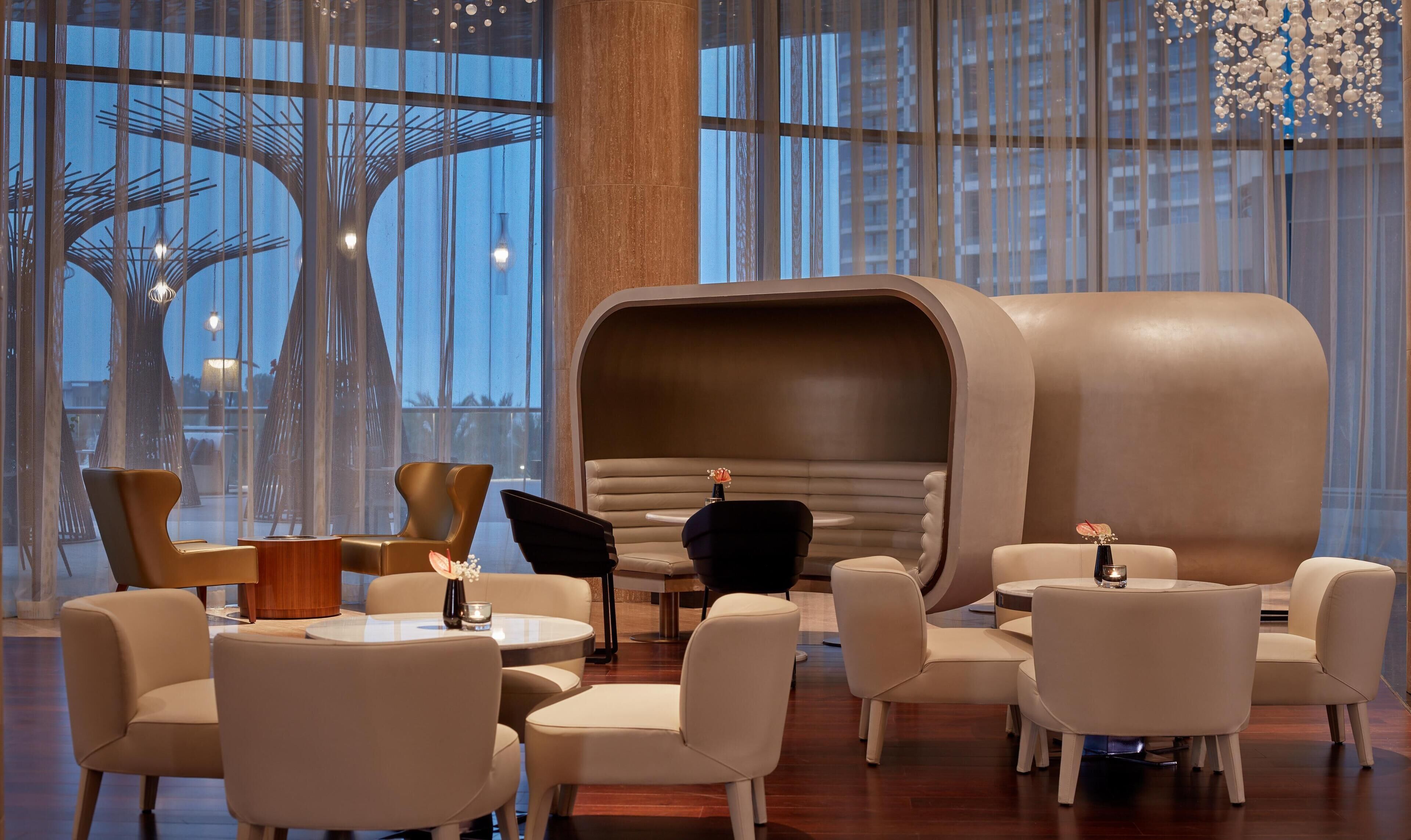 Un espace lounge moderne avec des sièges en cuir, un banc incurvé original et une vue sur le paysage urbain grâce à de grandes fenêtres.