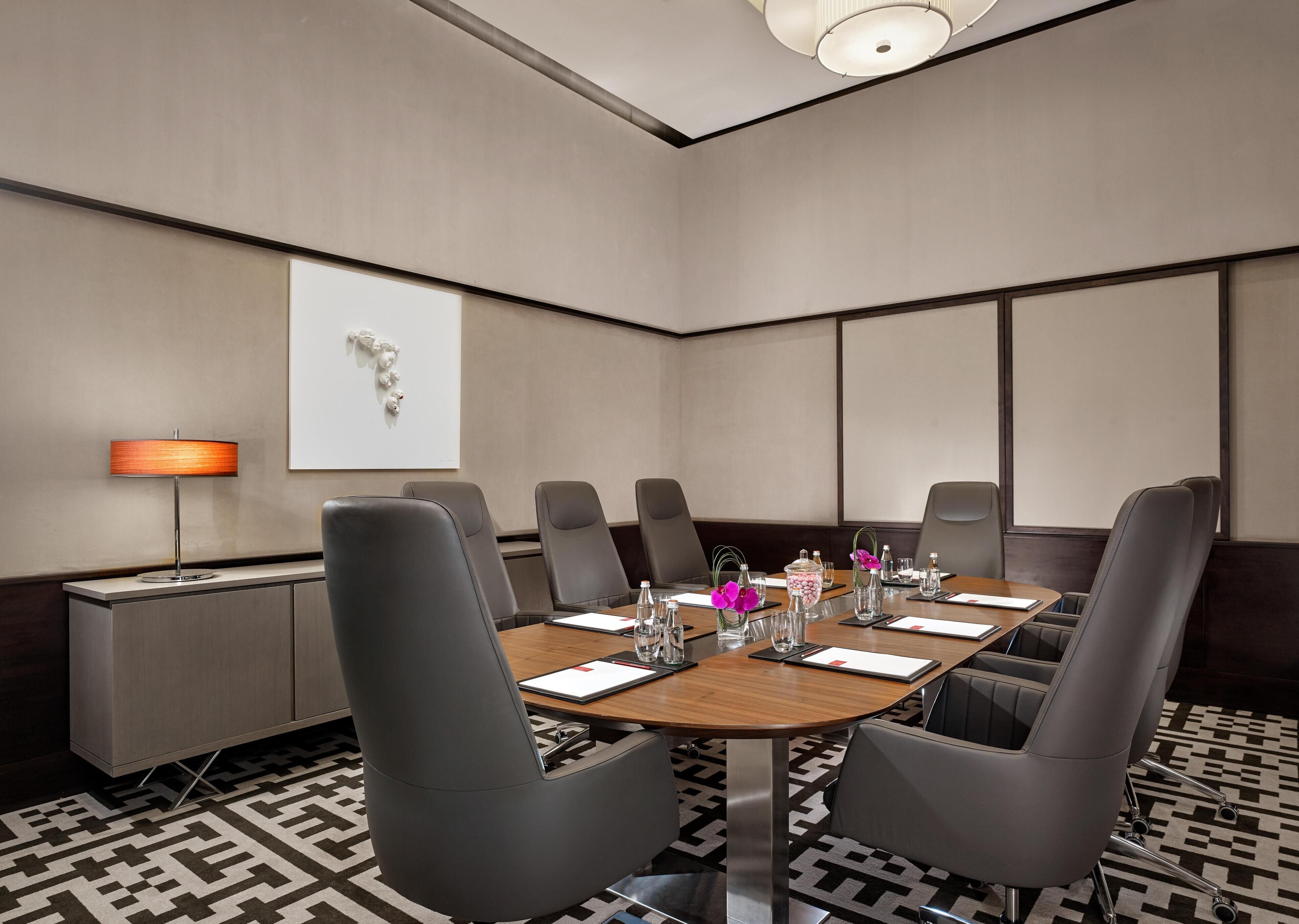 Ein Konferenzraum mit rundem Tisch, grauen Stühlen, einer Tafel und einer Lampe.