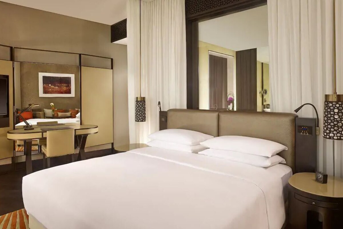 A hotel room with a large bed, a desk, a chair, a TV, and a mirror.