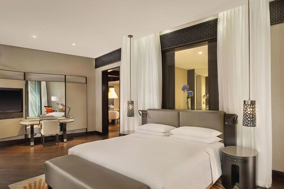 A hotel room with a large bed, a desk, a TV, and a mirror.