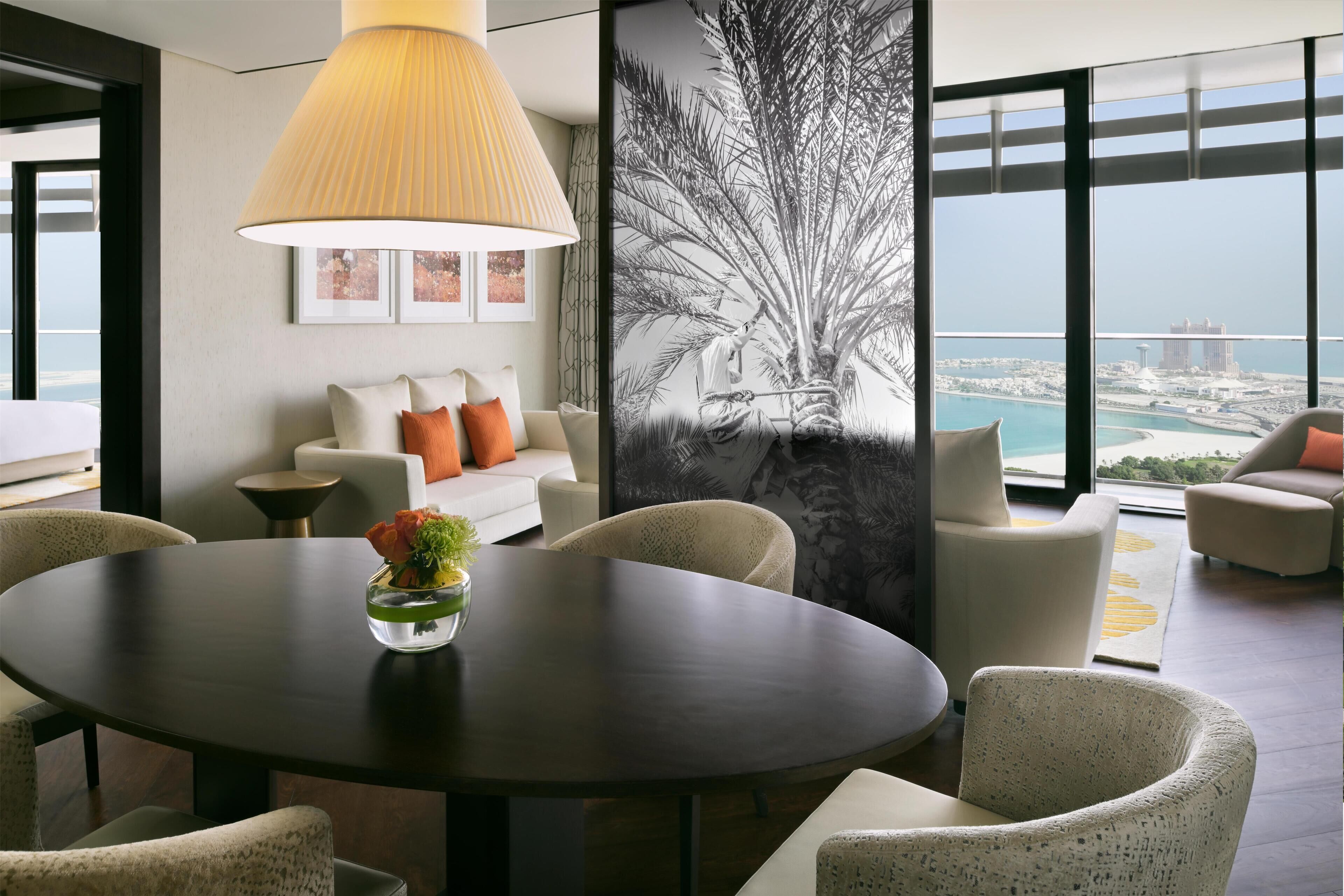 Ein modernes Wohnzimmer mit einem runden Tisch, gemütlicher Sitzgelegenheit, einem großen Fenster mit Blick auf die Stadt und einem gerahmten Kunstwerk an der Wand.