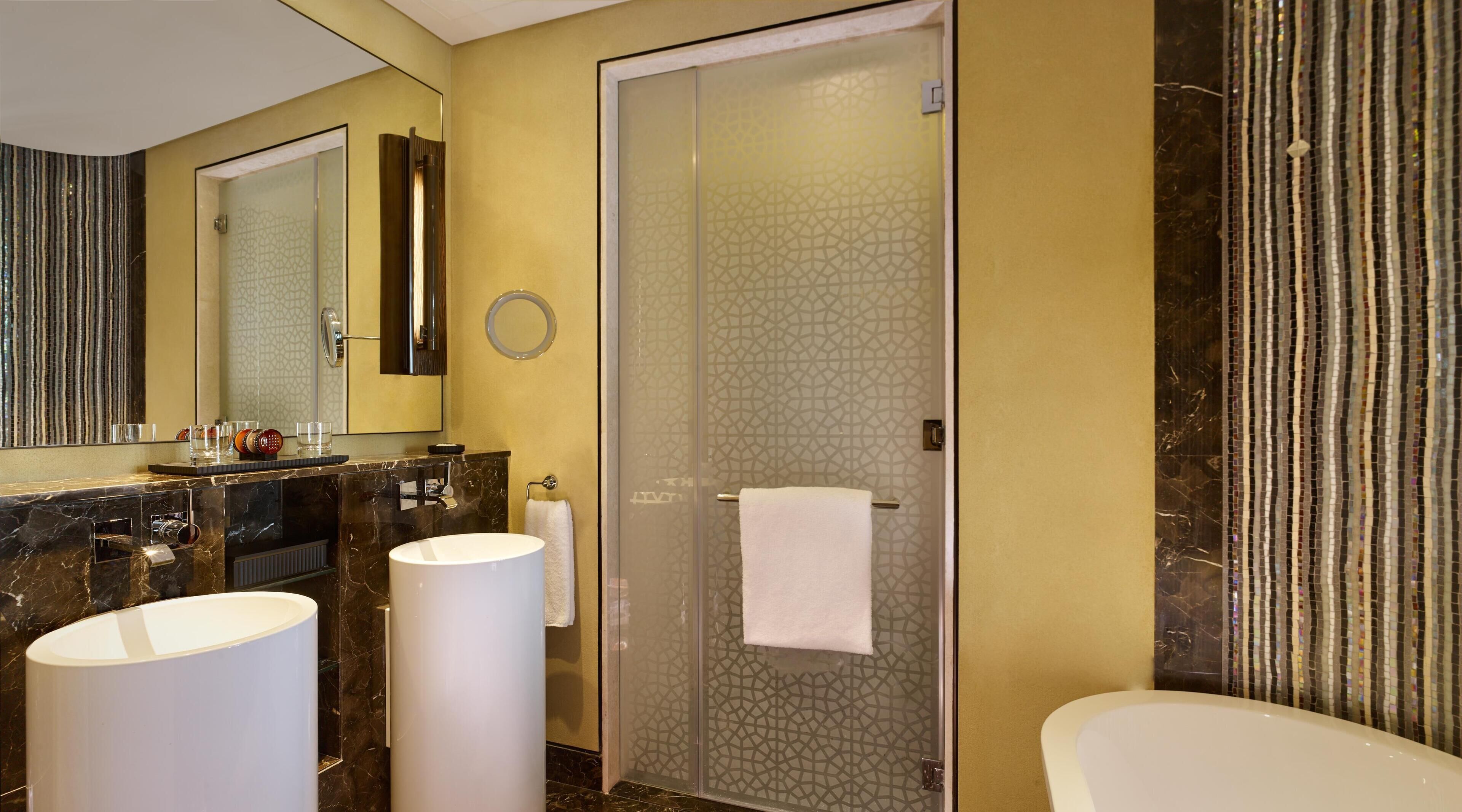 A modern bathroom with a marble vanity, two sinks, a large mirror, and a glass shower enclosure.