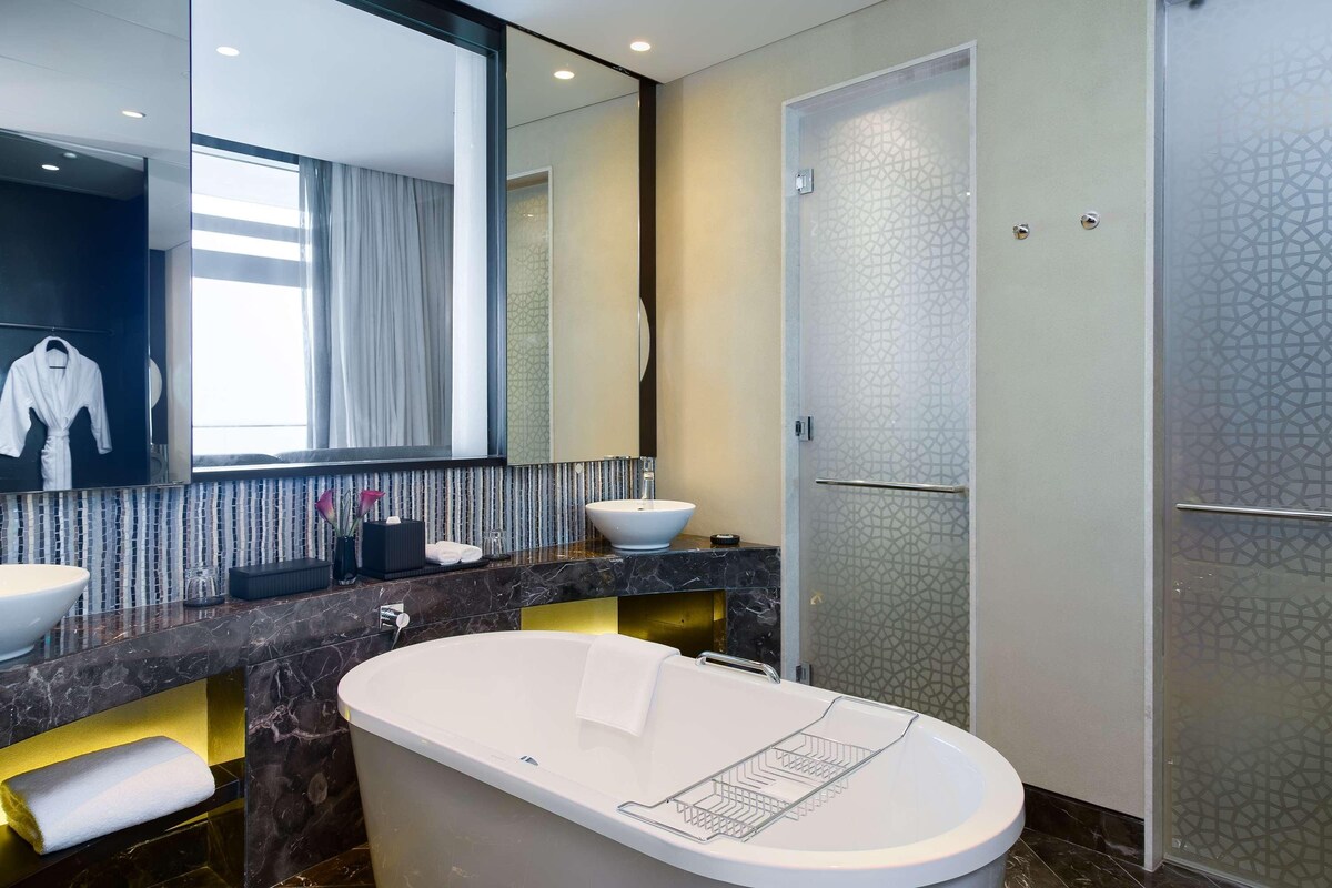 A modern bathroom with a freestanding bathtub, a large mirror, a vanity with a white sink, and a shower area.