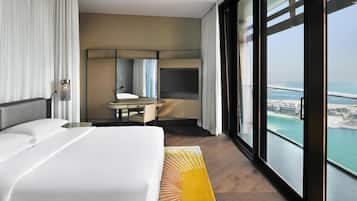 A hotel room with a bed, a desk, a large window with a view of the sea, and a modern interior design.