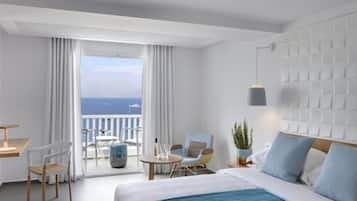 A modern hotel room with a balcony, a bed with blue bedding, a seating area with chairs, and a view of the sea.