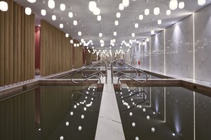 A modern indoor pool area with multiple lanes, clear water, and a central walkway.