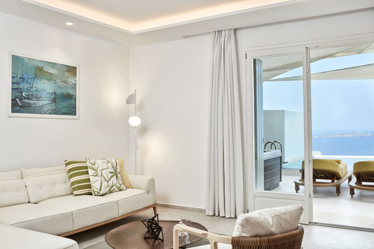 Ein modernes Wohnzimmer mit einem weißen Sofa, einem Gemälde und Meerblick durch eine Glastür.
