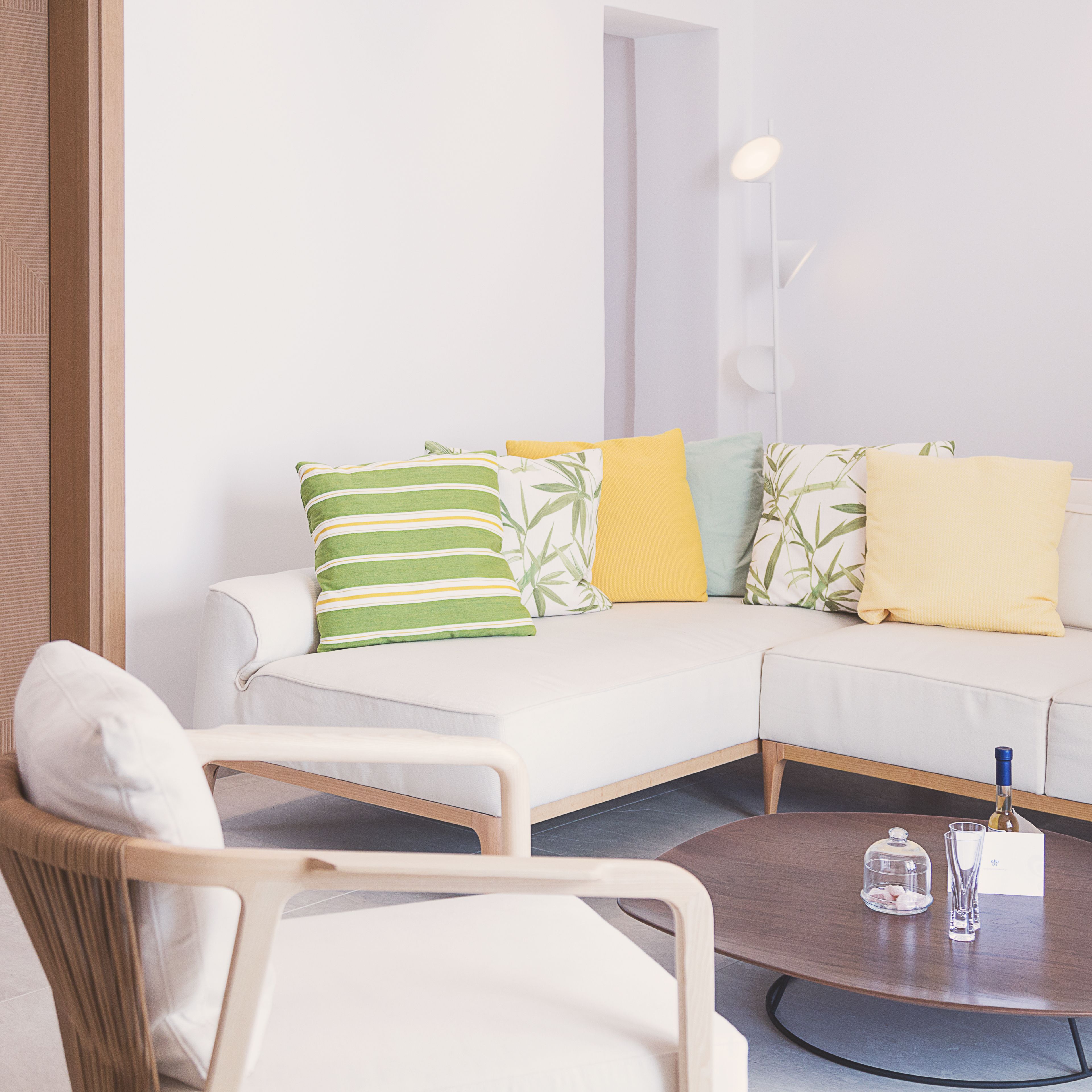 Una sala de estar moderna con un sofá blanco, una silla de madera y una mesa de centro con una cúpula de cristal y una botella.