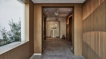 A modern hallway with wooden paneling, recessed lighting, and a view of a room with a sink and mirror.