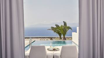 Vista de la piscina con mesa y sillas, una palmera y vistas al mar y las montañas.