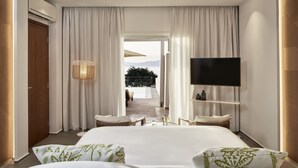 A modern hotel room with a large bed, a flat-screen TV, a ceiling light, and a view of the outdoors. - Myconian Korali Relais & Chateaux (Mykonos)