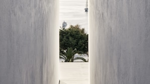 A corridor with a view of the sea and a distant mountain. - Myconian Korali Relais & Chateaux (Mykonos)