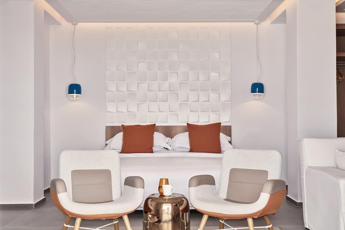 Ein modernes Hotelzimmer mit einem Bett, zwei Stühlen, einem kleinen Tisch und einer Wandleuchte.
