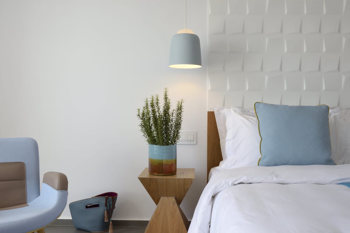 Ein modernes Schlafzimmer mit Bett, Sessel, Nachttisch, Lampe und einer Zimmerpflanze.