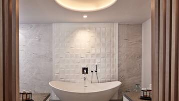 A modern bathroom with a freestanding bathtub, marble walls, and a recessed ceiling light.