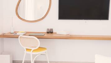 Een moderne werkplek met een houten bureau, een witte stoel met een geel kussen, een ronde spiegel en een zwart beeldscherm.