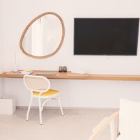 Un espacio de trabajo moderno con un escritorio de madera, una silla blanca con cojín amarillo, un espejo redondo y un monitor negro.