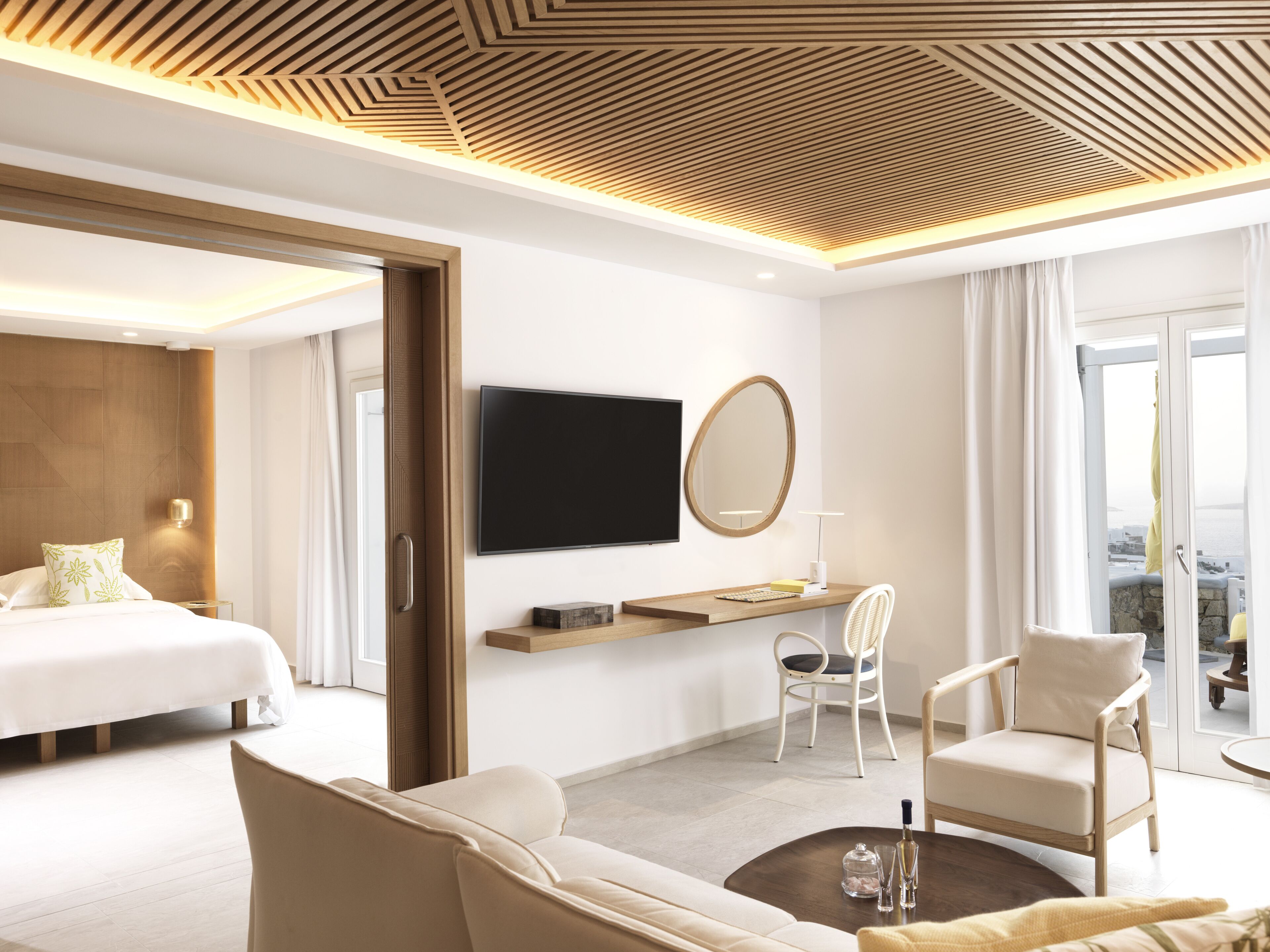 Una habitación de hotel moderna con una cama, un sofá, una silla, un televisor y un ventanal grande.