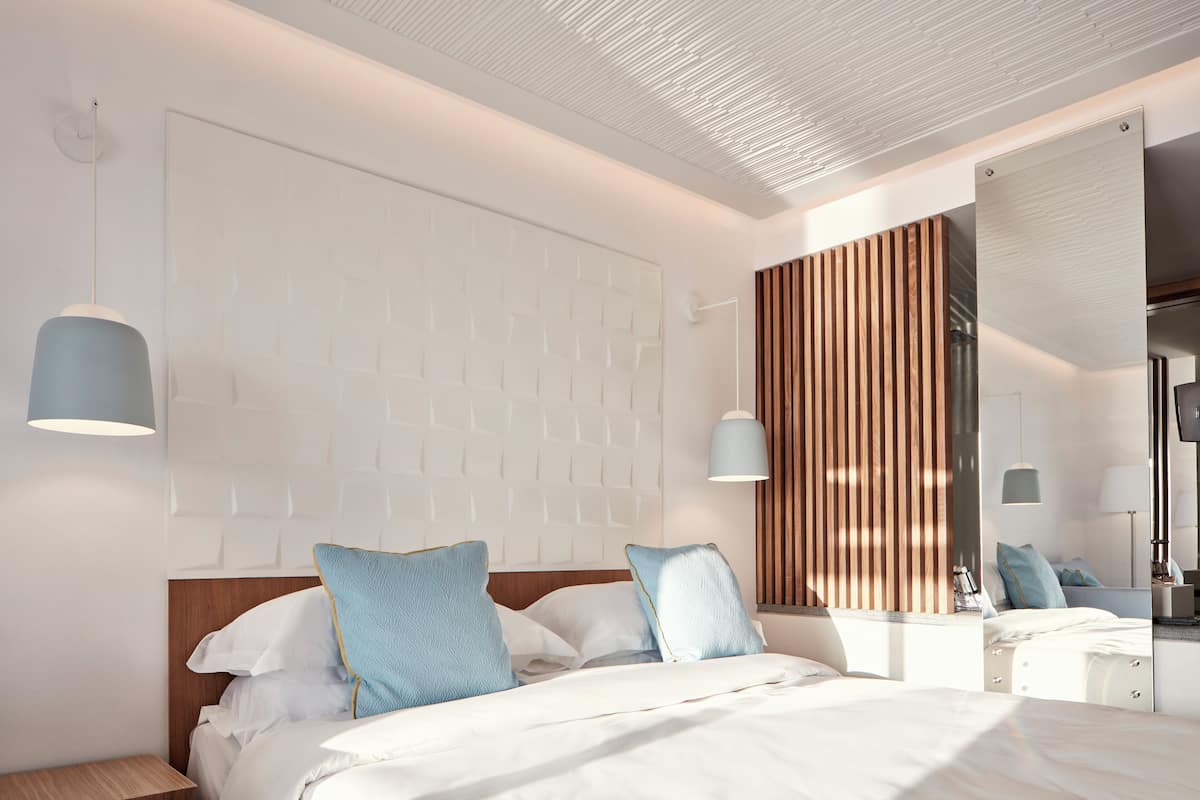 Ein modernes Schlafzimmer mit einem hölzernen Kopfteil, einem großen Spiegel und einem Bett mit weißen Laken und blauen Kissen.