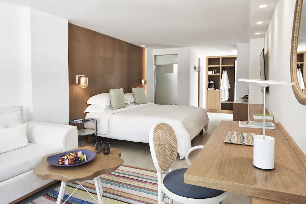 Ein modernes Hotelzimmer mit einem Bett, einer Couch, einem Esstisch und einem Spiegel.