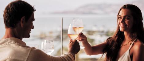 Een stel proost met wijnkoppen aan een tafel met uitzicht op zee.