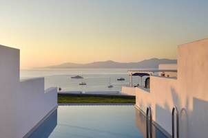 A modern building with a pool overlooking a calm sea with boats.