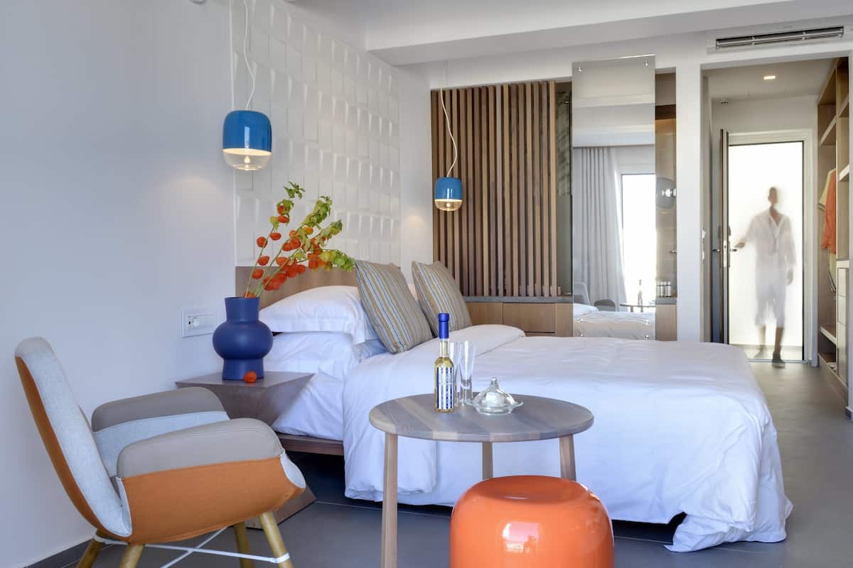 Ein modernes Hotelzimmer mit einem großen Bett, einem runden Tisch, einem Sessel und einem Nachttisch mit Blumen.