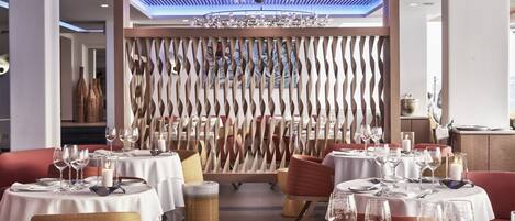 A restaurant with round tables set for dining, a decorative ceiling, and a wooden partition in the background.