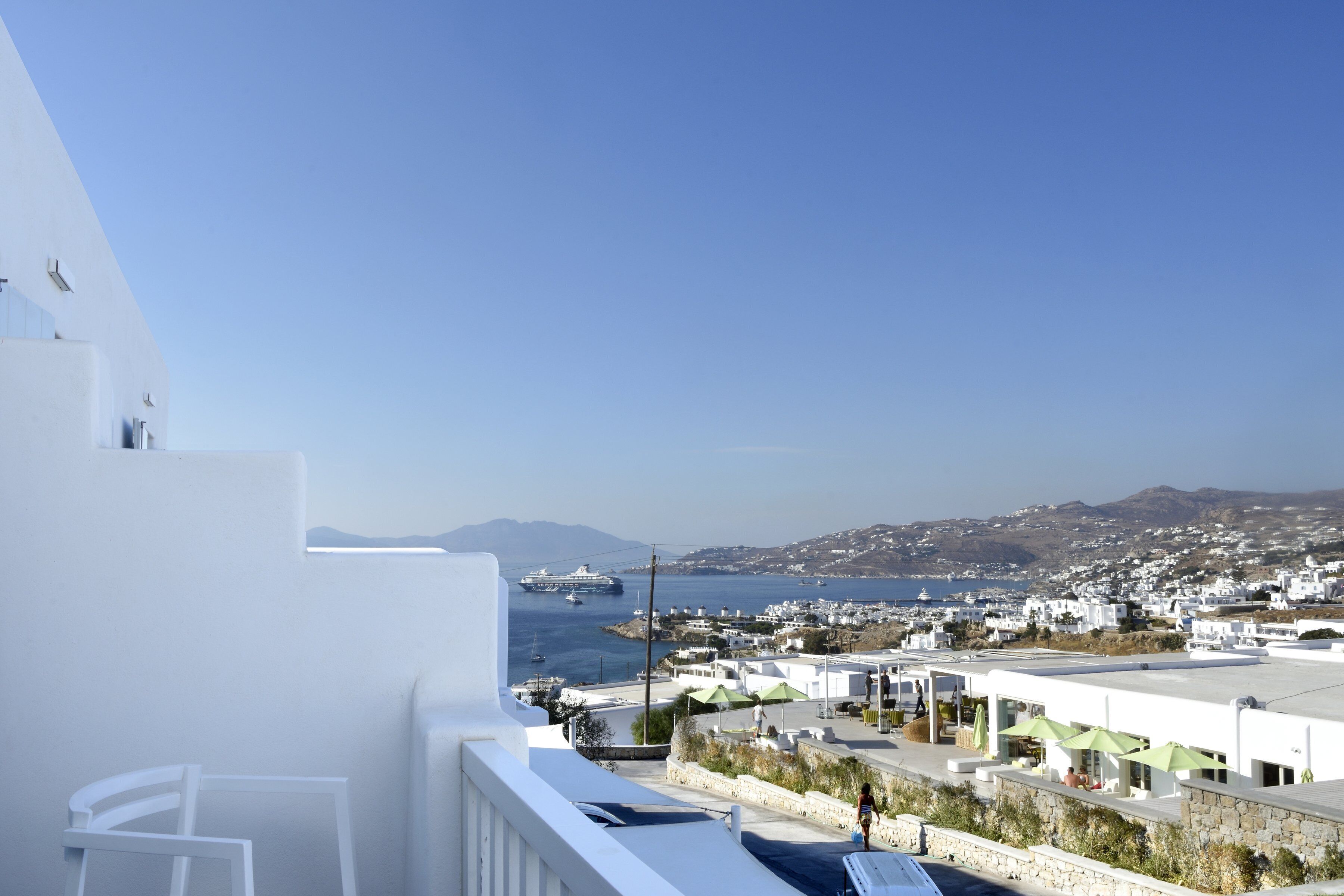 A balcony with a view of a coastal town, a clear sky, and a distant mountain range.