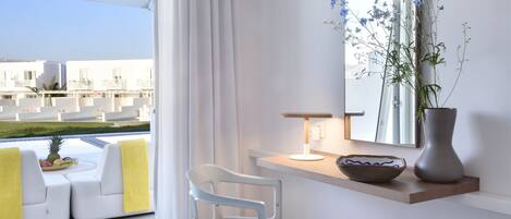 A modern room with a view of buildings, a white sofa, a chair, a table with a vase, and a bowl.