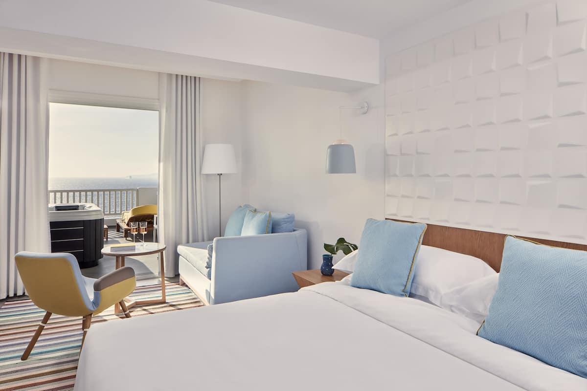 Ein Hotelzimmer mit einem großen Bett, einer Couch, einem Sessel, einem kleinen Tisch und Meerblick.