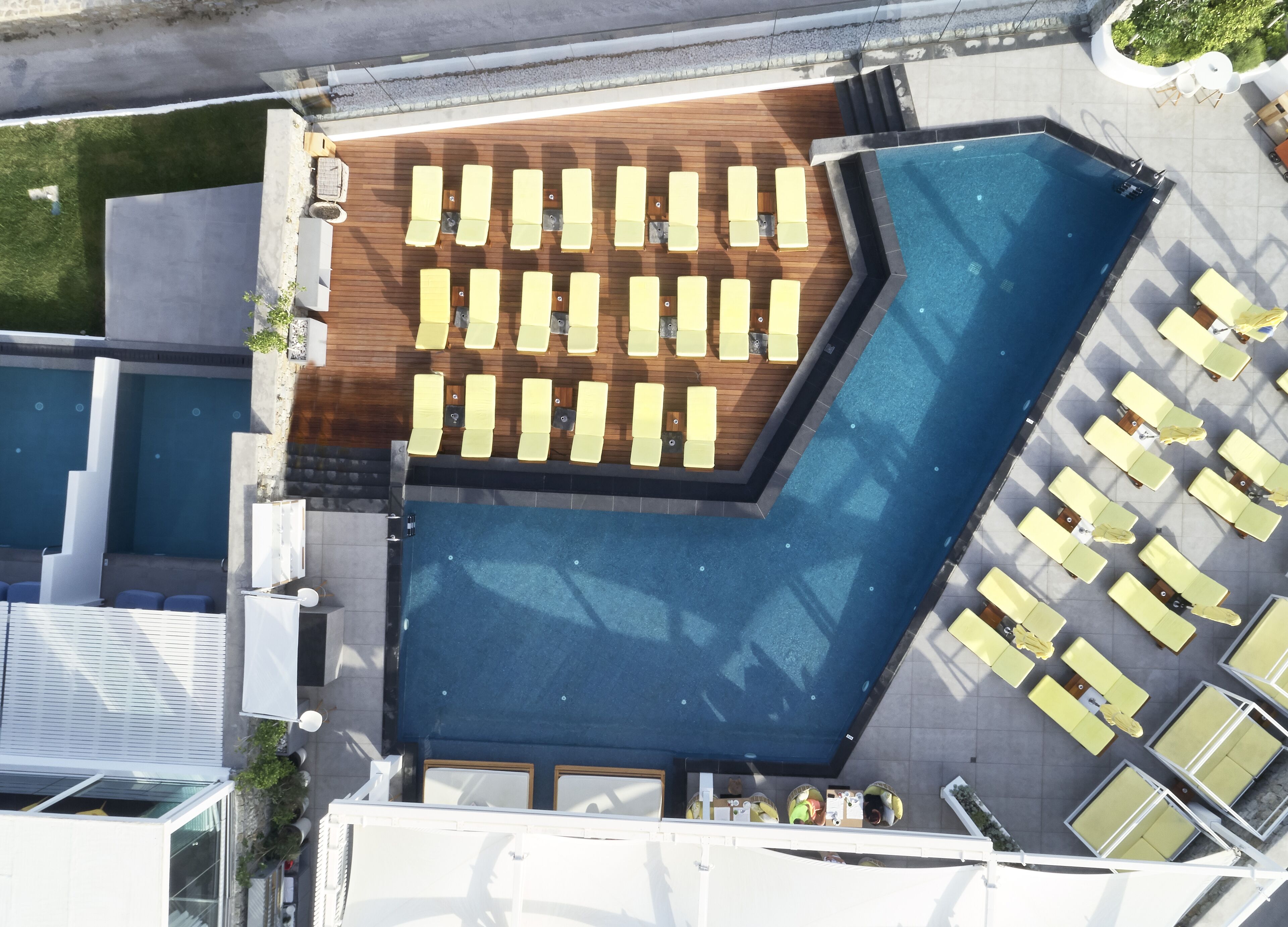 Vista aérea de un área de piscina con múltiples tumbonas dispuestas alrededor, una terraza de madera y un espacio de relax con sillas.