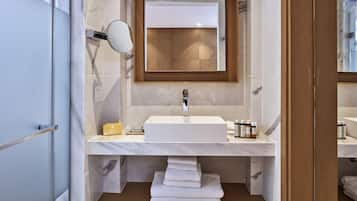 Ein modernes Badezimmer mit einem weißen Waschbecken, Marmorfliesen, einem Holz-Waschtisch und einem Spiegel darüber.