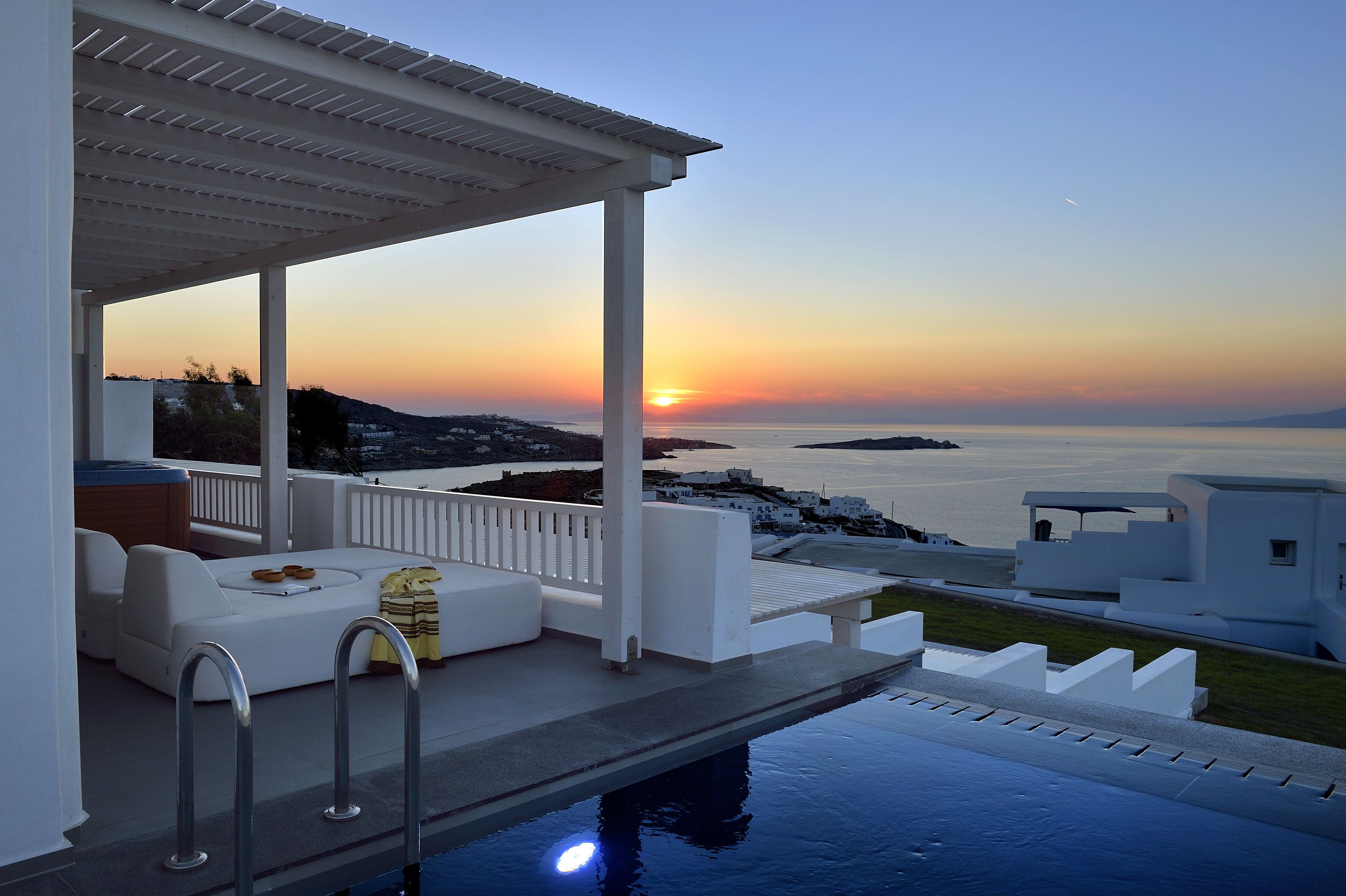 Uma área de estar externa com piscina, com vista para o pôr do sol sobre o mar.