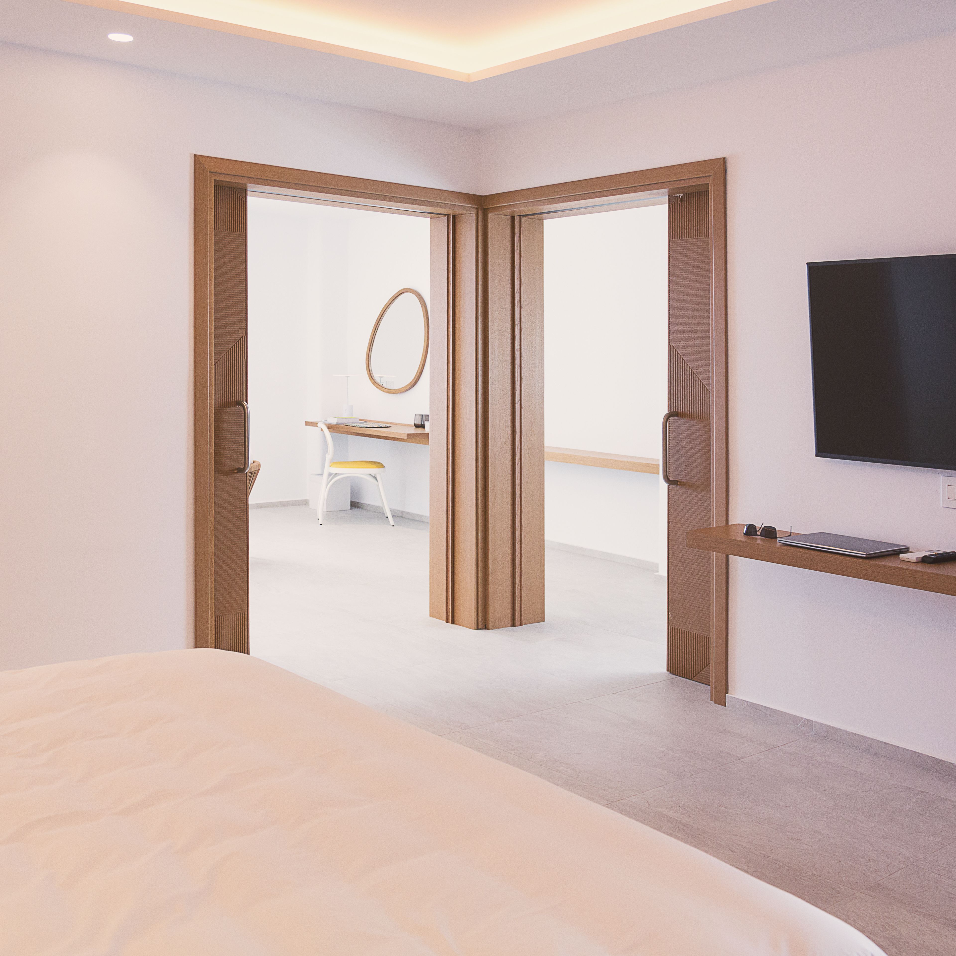 Una habitación de hotel moderna con una cama, un escritorio con una silla, un espejo y un televisor en la pared.