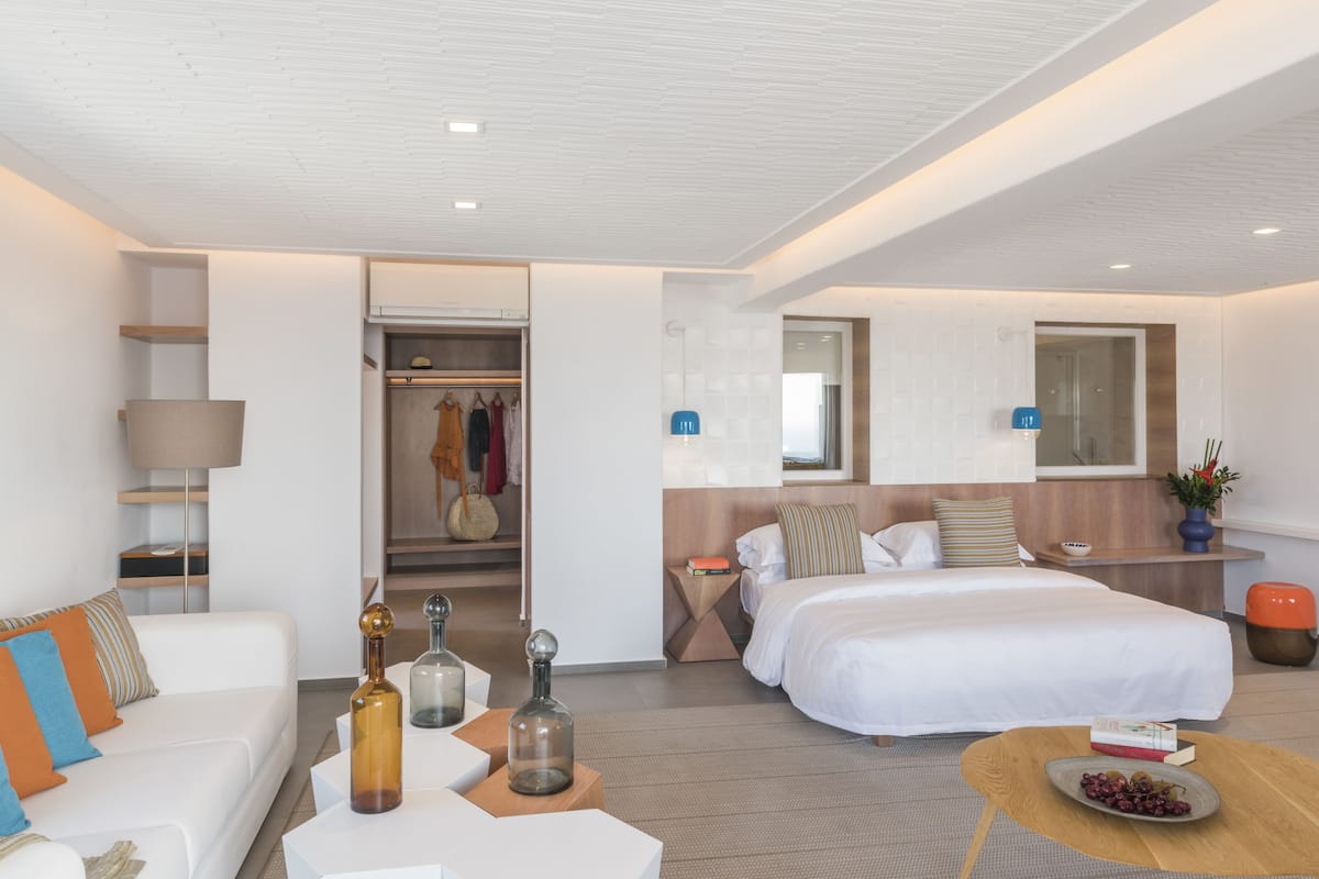 Ein modernes Hotelzimmer mit einem weißen Sofa, einem Bett, einem Nachttisch mit Lampe und einem kleinen Beistelltisch mit Dekoration.