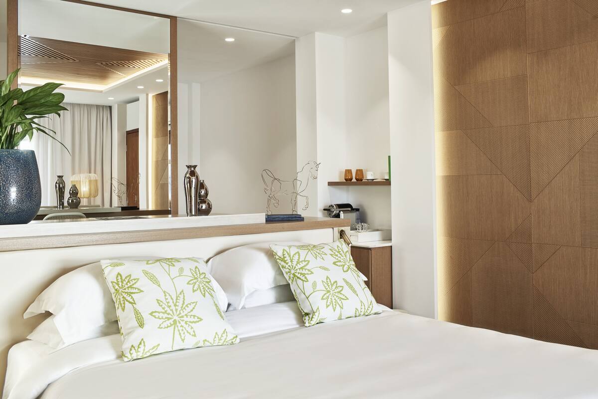 Ein Hotelzimmer mit einem Bett, einem großen Spiegel, einer Pflanze und einer Wandpaneele aus Holz.
