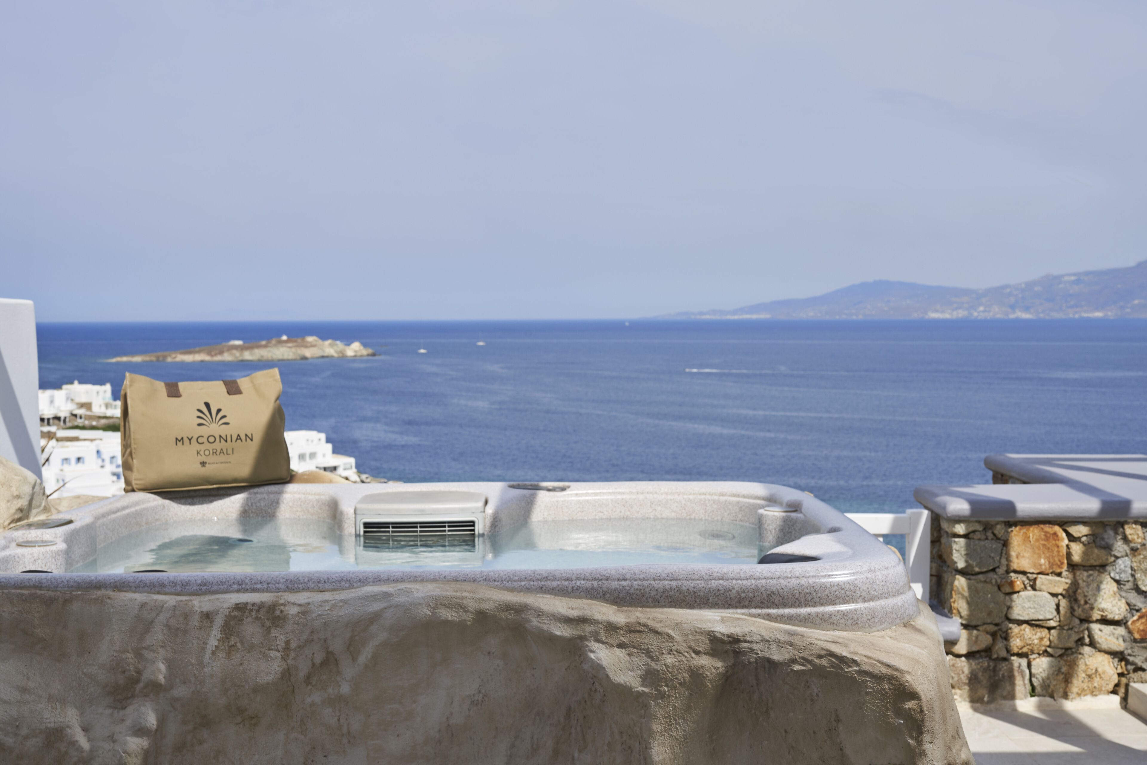 A hot tub with a view of the sea and a bag labeled "MYCONIAN KORALI".