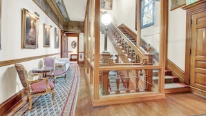 A grand hallway with ornate woodwork, a staircase with a glass railing, and a chandelier. - The Gables at Stirling Guest Hotel (Reading)