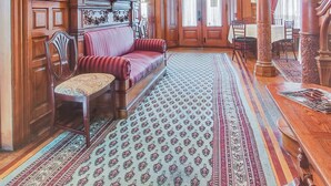 A grand room with ornate woodwork, a patterned carpet, and a red upholstered sofa. - The Gables at Stirling Guest Hotel (Reading)