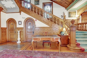 A grand staircase with ornate woodwork, a large wooden table with a chair, and a patterned rug on the floor. - The Gables at Stirling Guest Hotel (Reading)