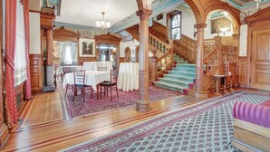 A grand hall with a staircase, wooden columns, and a dining area with tables and chairs. - The Gables at Stirling Guest Hotel (Reading)