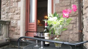 A table with a wine bottle, glasses, and a vase of flowers outside a building with stone walls and a red door. - The Gables at Stirling Guest Hotel (Reading)