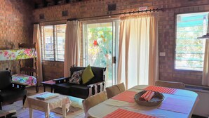 Ein gemütliches Zimmer mit Backsteinwand, einer hölzernen Bank, einer Couch, einem Esstisch mit Platzsets und einem Fenster mit Vorhängen.